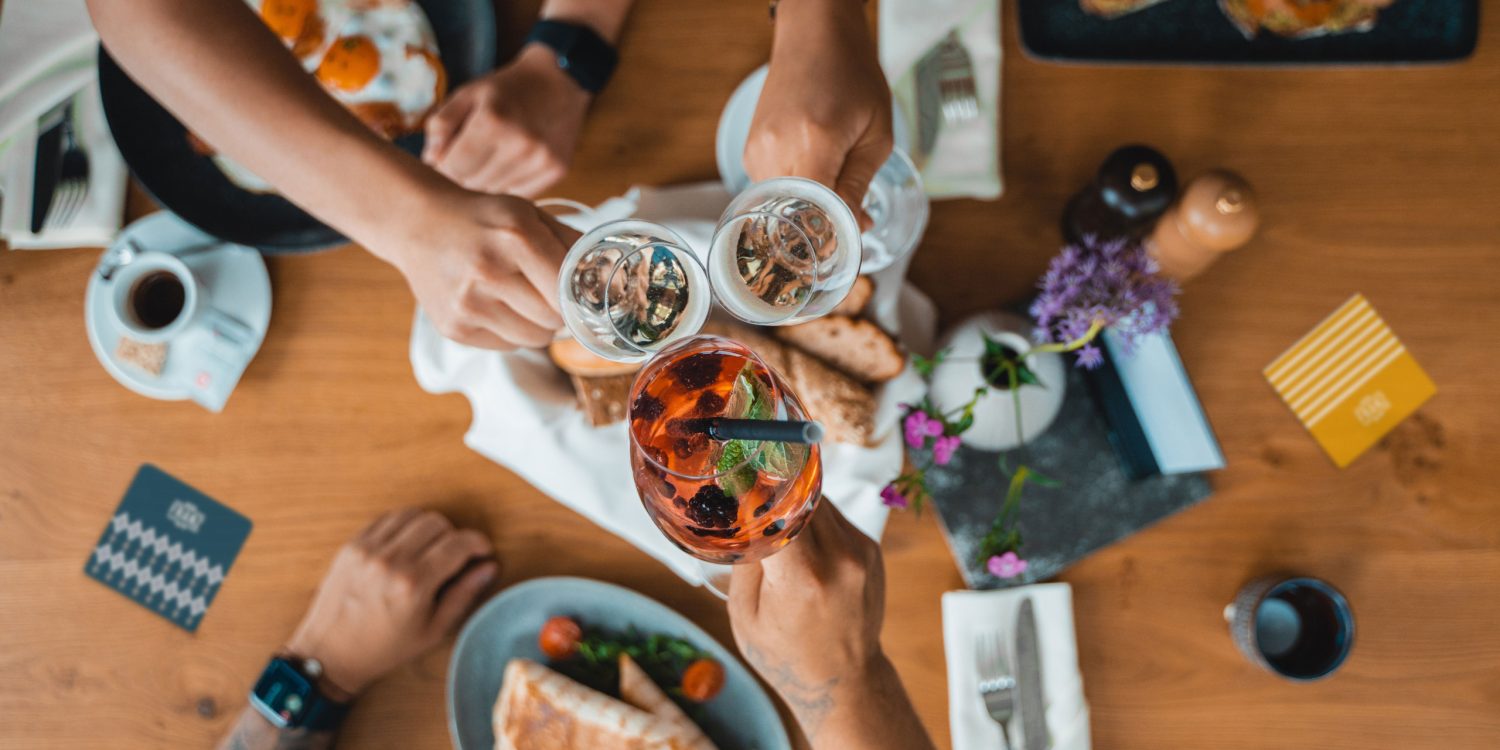 A group of people toasting at a table with food and drinks.