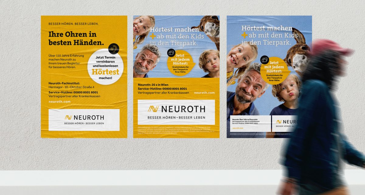 Eine Gruppe von Menschen geht mit Plakaten an der Wand, die für Neuroth Hörgeräte werben, einen Bürgersteig entlang.