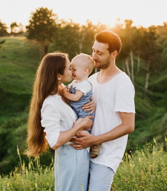 A couple kissing their baby in a field at sunset in Kinderhotels.