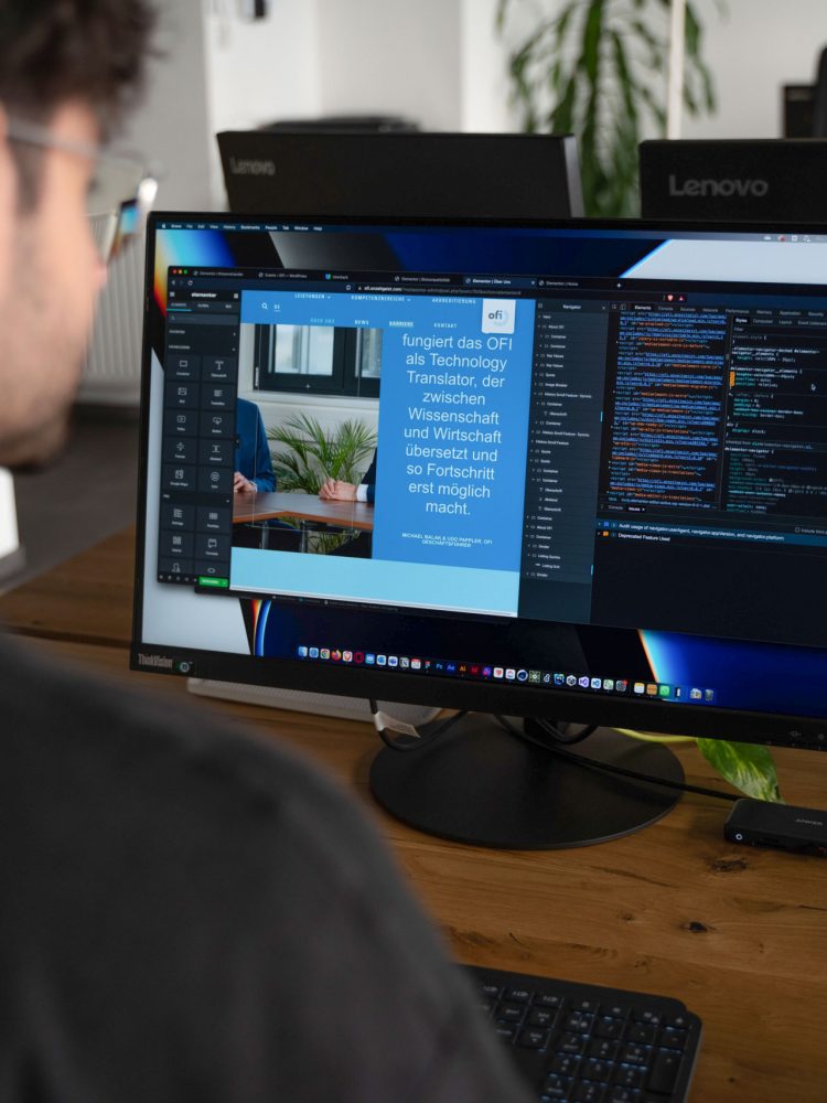 A man sitting at a desk with two monitors in front of him.