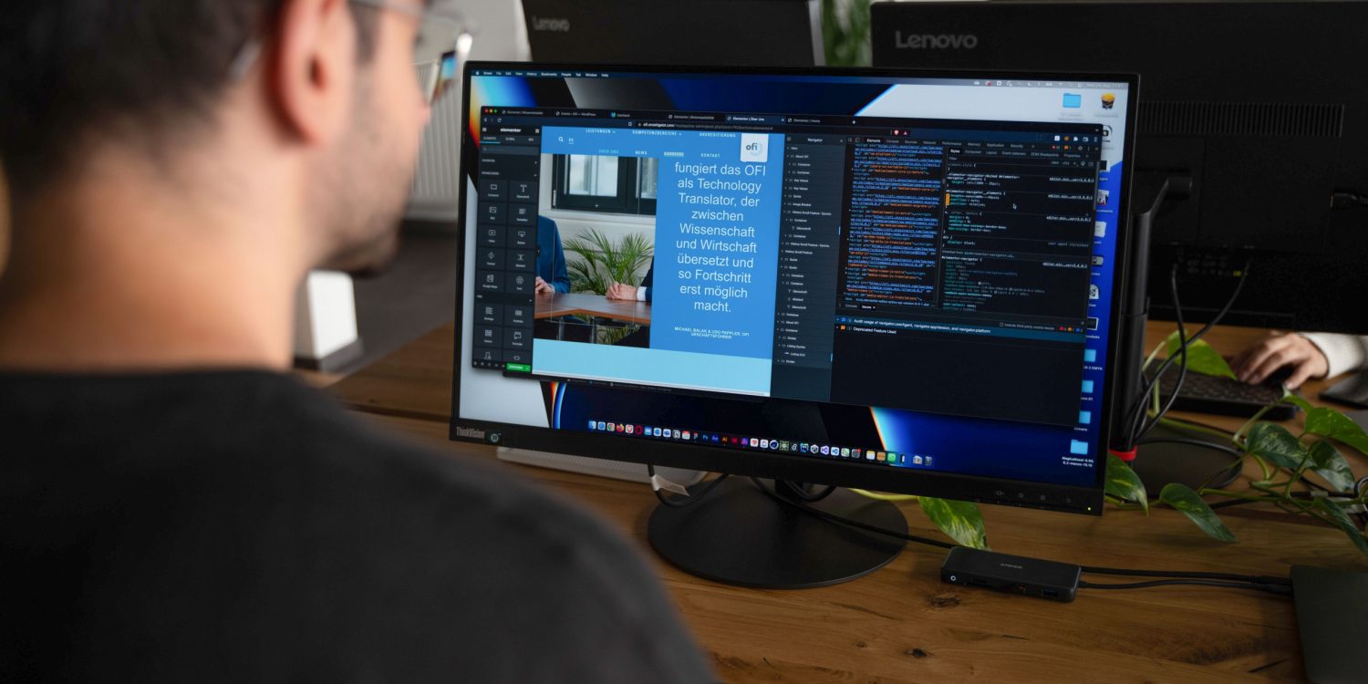 A man sitting at a desk with two monitors in front of him.